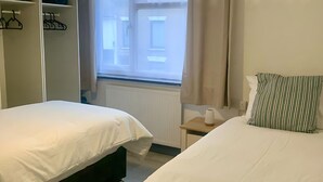 A bedroom with two beds, a wardrobe, a radiator, and a window with curtains. - Cosy 3-Bed Home in Central Colchester (Colchester)