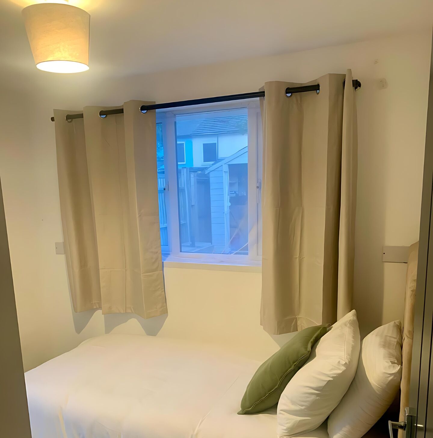 Un dormitorio con cama, una ventana con cortinas y una lámpara en el techo.