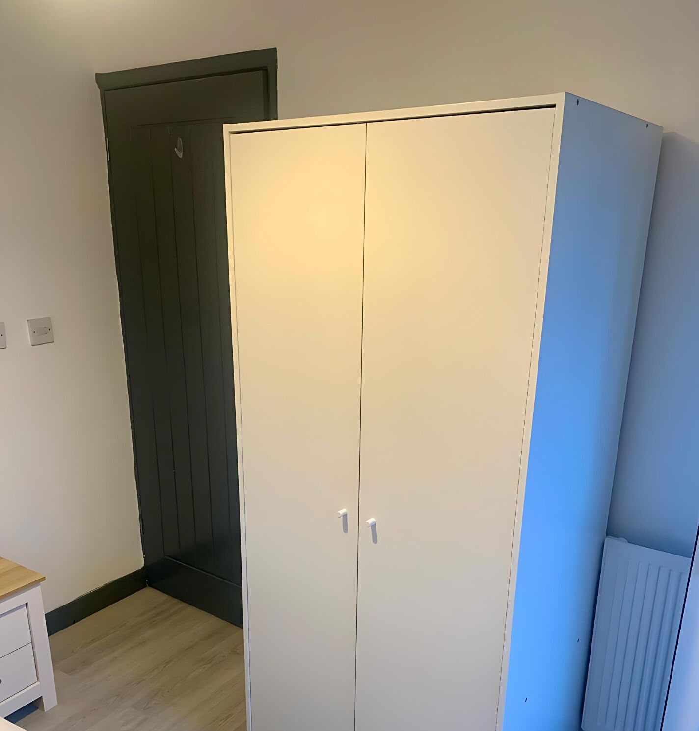 A room with a white wardrobe, a dark door, and a light-colored floor.