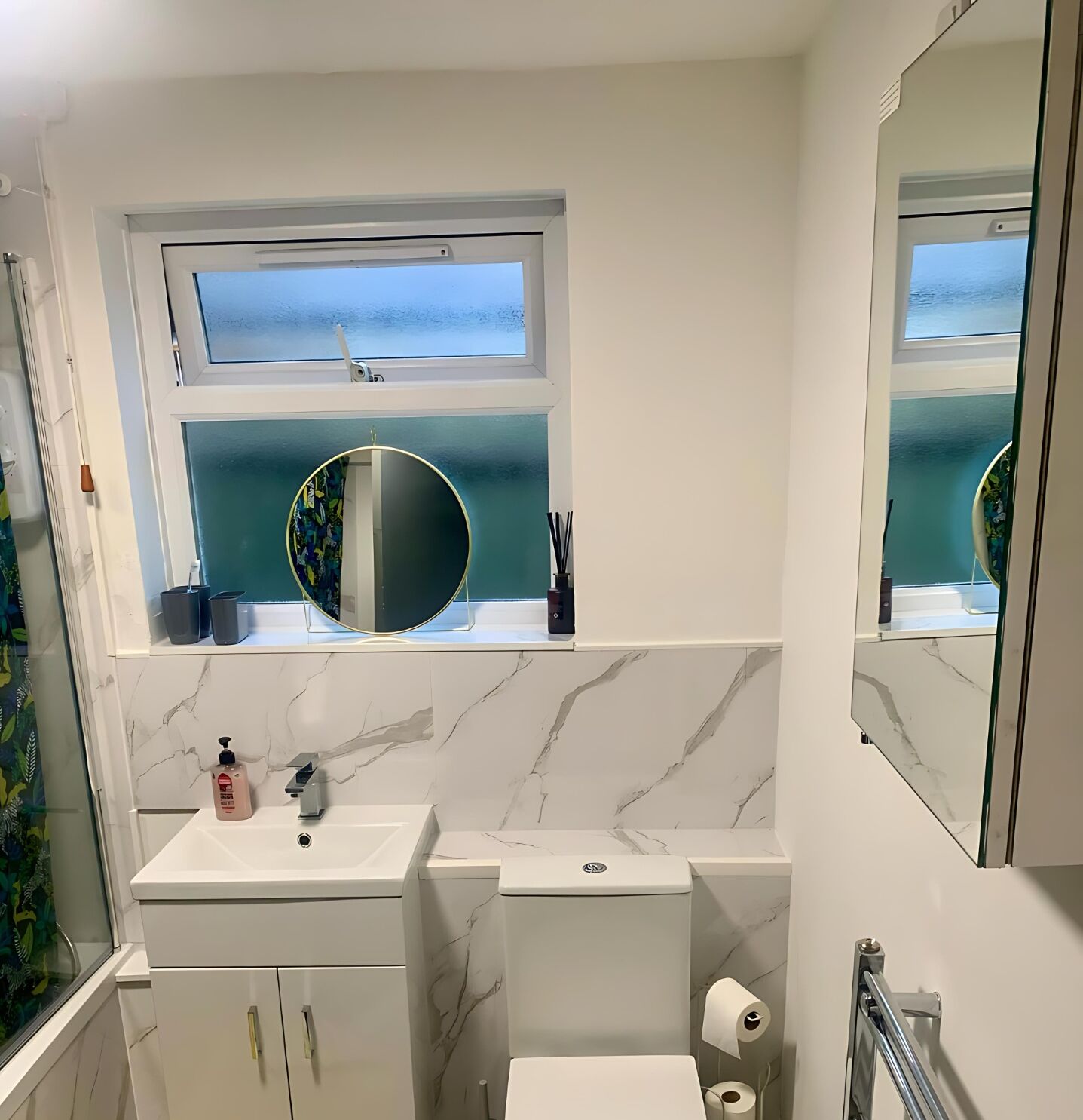 A bathroom with a white marble sink, a toilet, a window with a view of the sea, and a mirror.