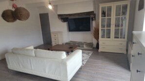 Un salón con un sofá blanco, una mesa de centro de madera, un televisor de pantalla plana montado en la pared y un aparador con puertas de cristal.