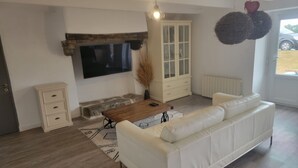 Un salón con sofá blanco, una mesa de centro de madera y un televisor montado en la pared.