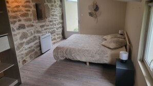Un dormitorio con pared de piedra, una cama con ropa de cama estampada, una mesita de noche con una lámpara y una ventana con vistas.