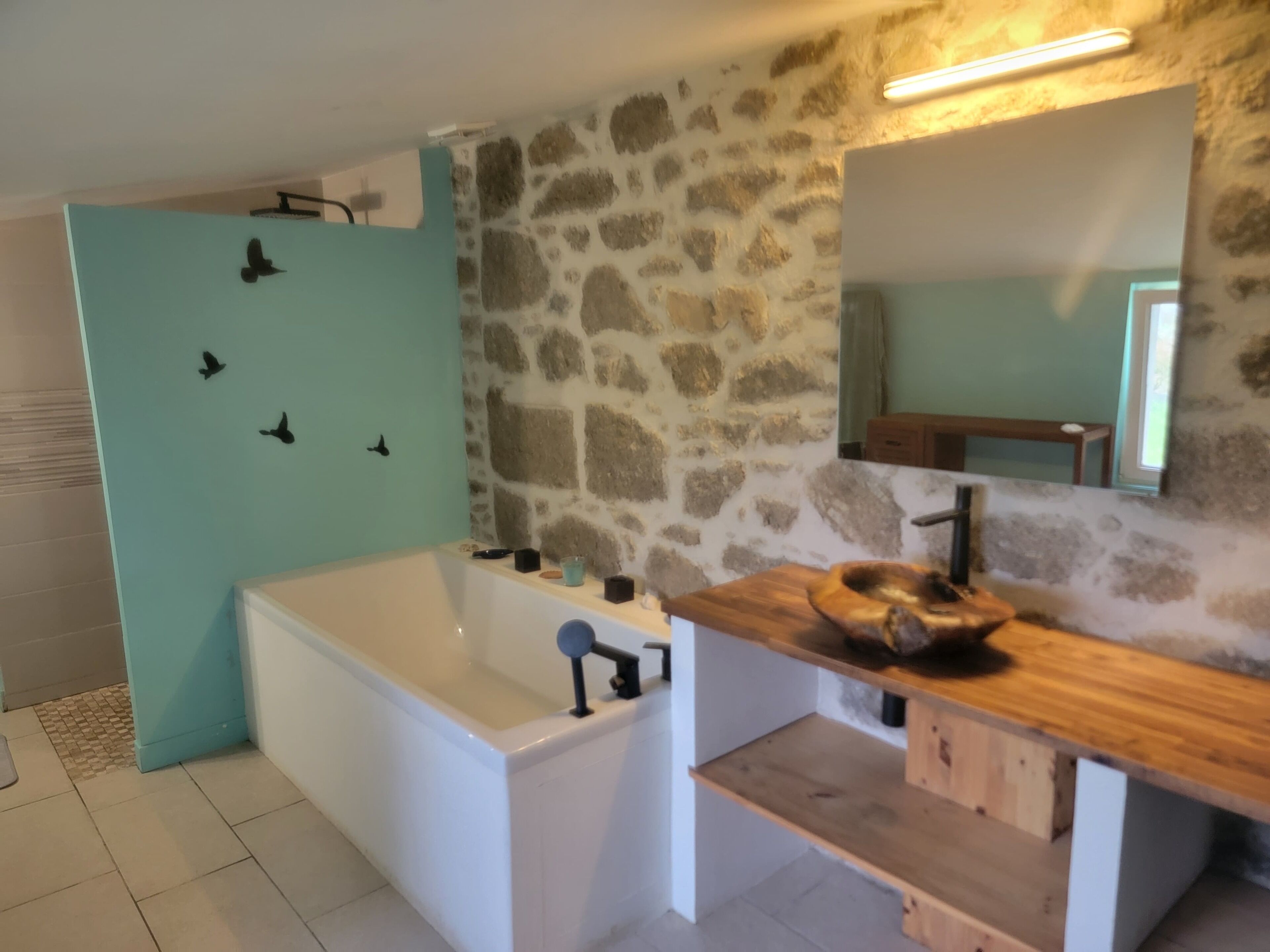A bathroom with a stone wall, a white bathtub, a wooden vanity, and a mirror.