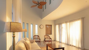 Uma sala de estar ampla com um sofá, duas poltronas, uma mesa de centro, uma luminária e um ventilador de teto.