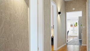 Un pasillo con papel tapiz estampado, suelo de madera y una puerta que da a otra habitación.