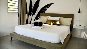 Cama bem arrumada com edredom branco e travesseiros, mesa de cabeceira com abajur e uma grande decoração de parede com padrões de folhas pretas.