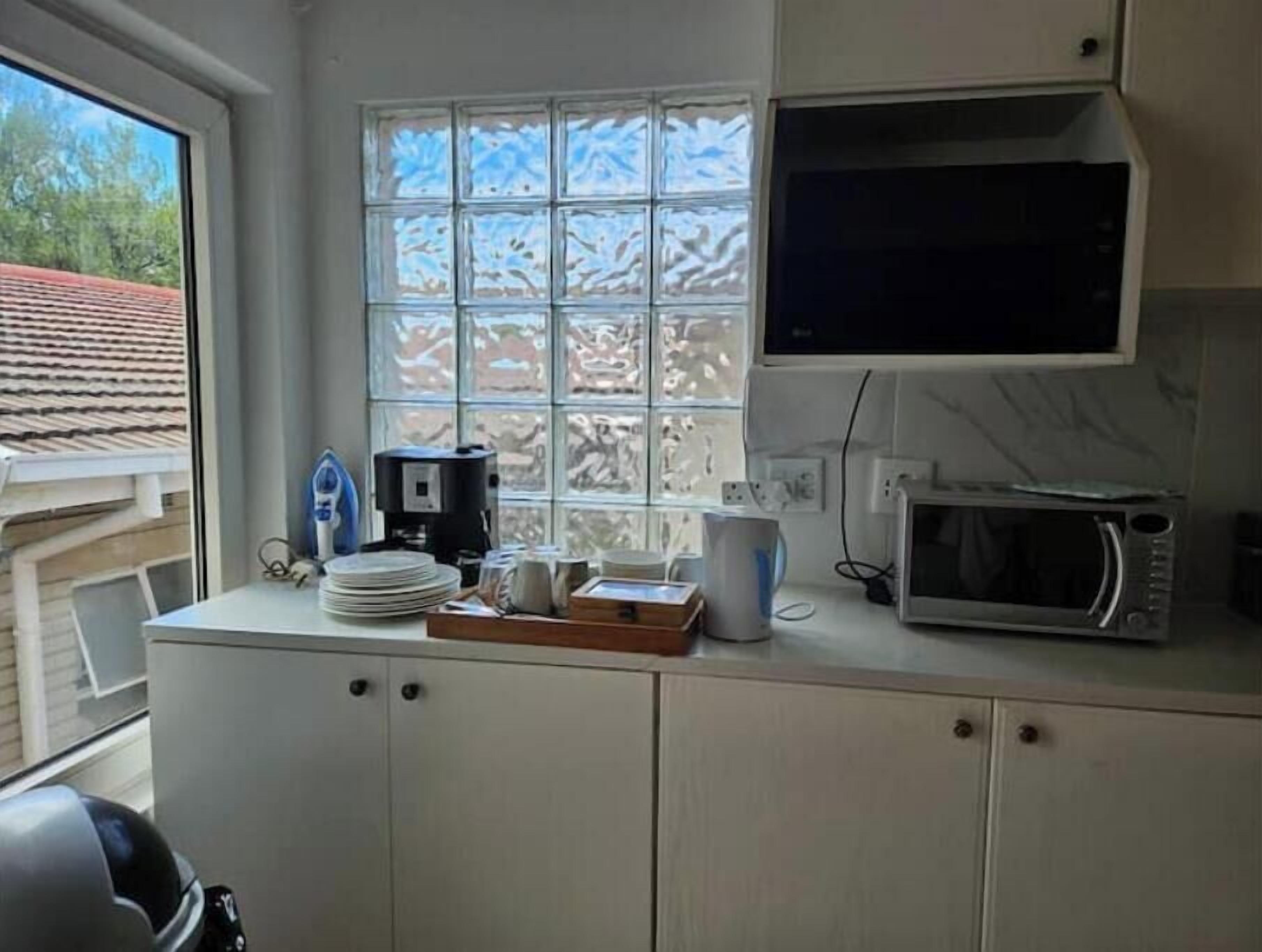 Een keuken met een raam, een magnetron, een koffiezetapparaat en een waterkoker.