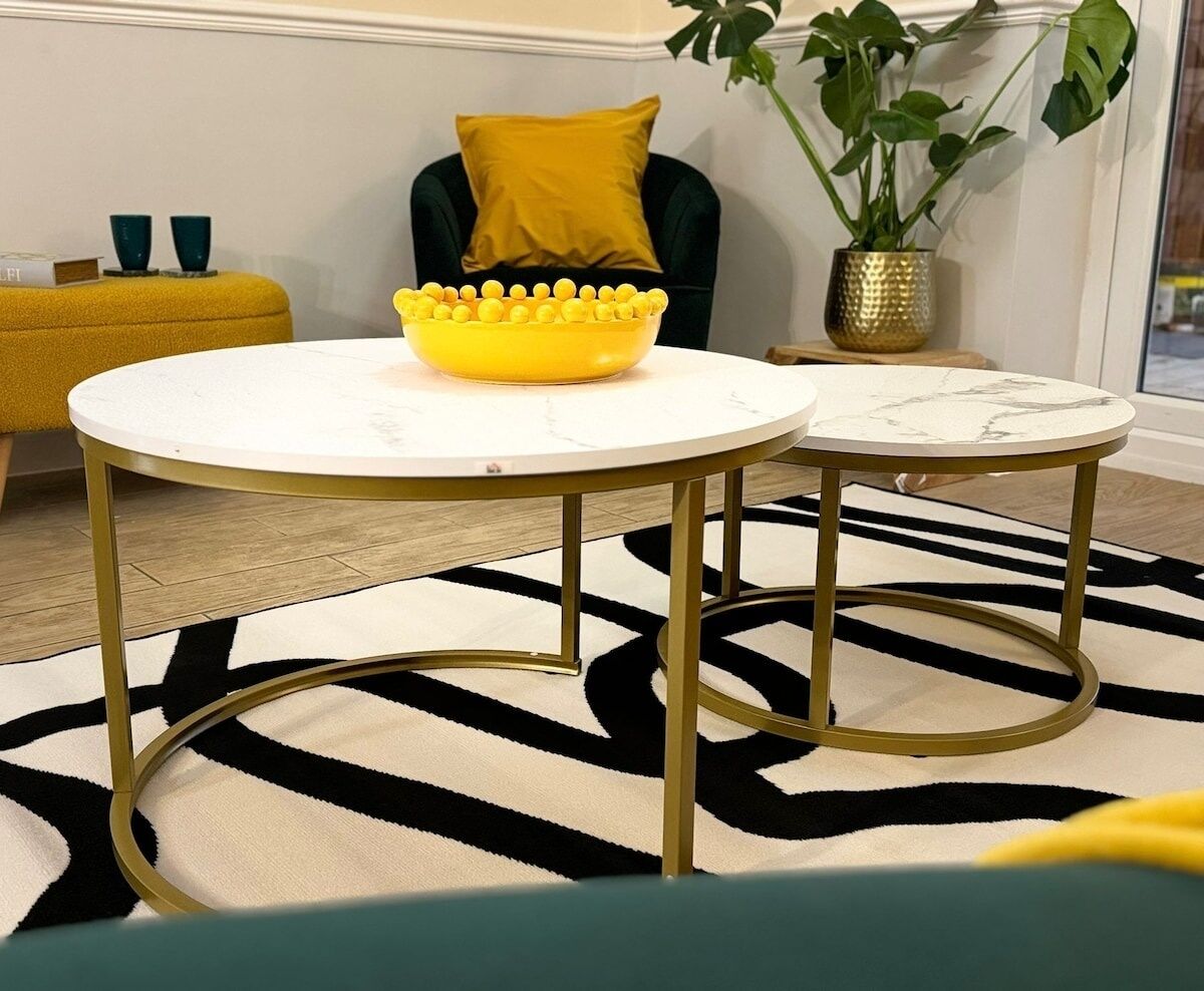 A room with two round tables with gold legs, a yellow bowl on one table, a green chair, and a plant in a gold pot.