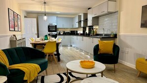 Une cuisine moderne avec des meubles blancs, un plan de travail noir et un saladier jaune posé sur une table blanche.