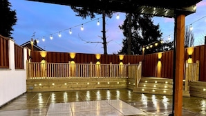 Un espace extérieur aménagé en terrasse, avec une plateforme en bois, un sol en pierre et des guirlandes lumineuses.