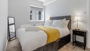 A modern bedroom with a bed, bedside table, and a window. - Modern Apartment 2 Double Bed Free Parking Suite11 (Nottingham)