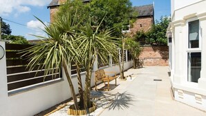 A courtyard with a bench, palm trees, and a white building with a brick wall and a solar panel. - Modern Apartment 2 Double Bed Free Parking Suite11 (Nottingham)