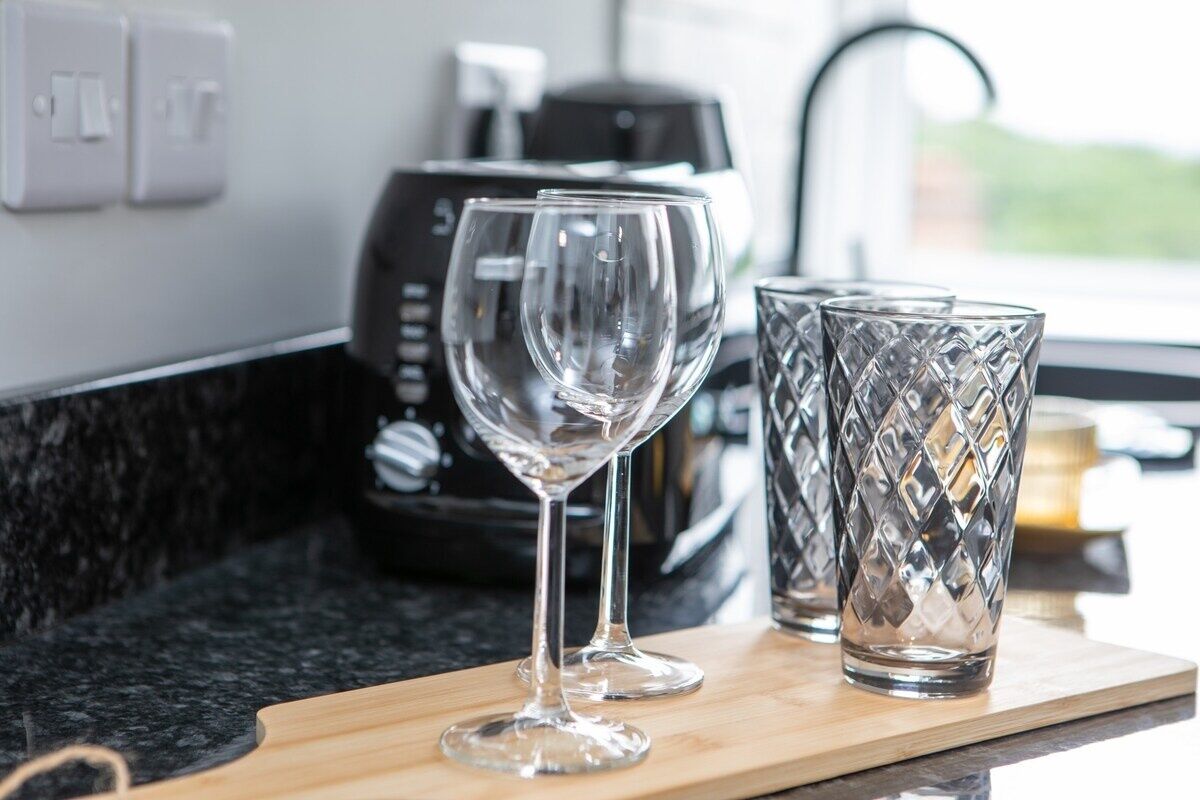 Una encimera de cocina con una cafetera, dos copas de vino y un recipiente de vidrio.