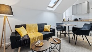 A modern living room with a sofa, coffee table, and lamp, a kitchen area with cabinets and appliances, and a skylight above the sofa. - Modern Apartment King Room |Free Parking| Suite 9 (Nottingham)