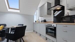 A modern kitchen with grey cabinets, a black microwave, and an oven. There is a dining area with a table and chairs. - Modern Apartment King Room |Free Parking| Suite 9 (Nottingham)