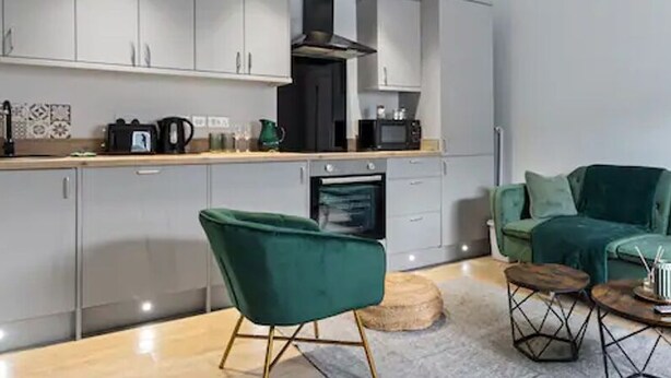 A modern kitchen with grey cabinets, a green sofa, and a dining area with a round table and chairs. - Modern Apartment Double Bed |Free Parking |Suite 7 (Nottingham)