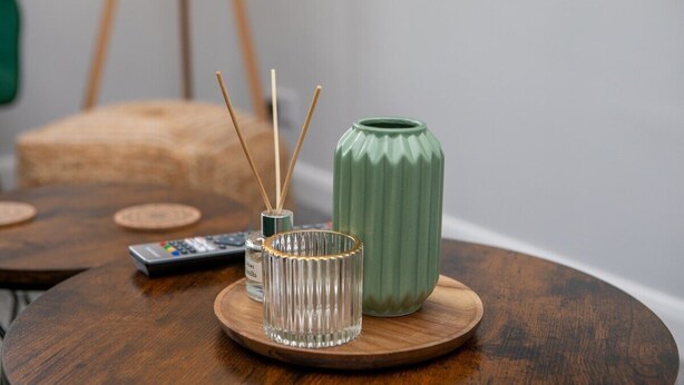 A round wooden table with a green vase, a glass candle holder, and a remote control. - Modern Apartment| King Bed| Free Parking |Suite 6 (Nottingham)