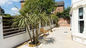 Une cour avec un banc, des palmiers et un bâtiment blanc doté d’un mur en briques.