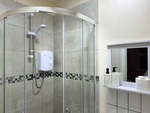 Een moderne badkamer met een douchecabine van glas, een toiletrolhouder en een spiegel.