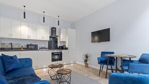 A modern kitchen with white cabinets, a black range hood, and a microwave. There is a dining area with blue chairs and a round table. - Modern Apartment Double Bed |Free Parking| Suite 4 (Nottingham)