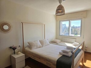 A bedroom with a wooden four-poster bed, a bedside table, a radiator, and a window with a view of trees. - Casa Buen Camino Arzúa (Arzúa)