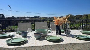 Una mesa dispuesta para comer, con platos, cuencos y vasos verdes, y un jarrón con flores secas.