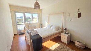 Un dormitorio con cama, mesita de noche, lámpara y vistas a través de la ventana.