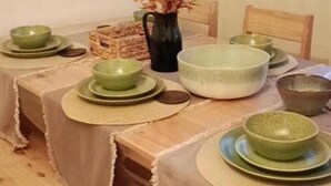 Una mesa de comedor dispuesta con platos y tazones verdes, un tazón blanco grande y un jarrón con flores secas.