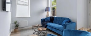 Une pièce avec un canapé bleu, deux petites tables rondes, une lampe et une plante en pot.