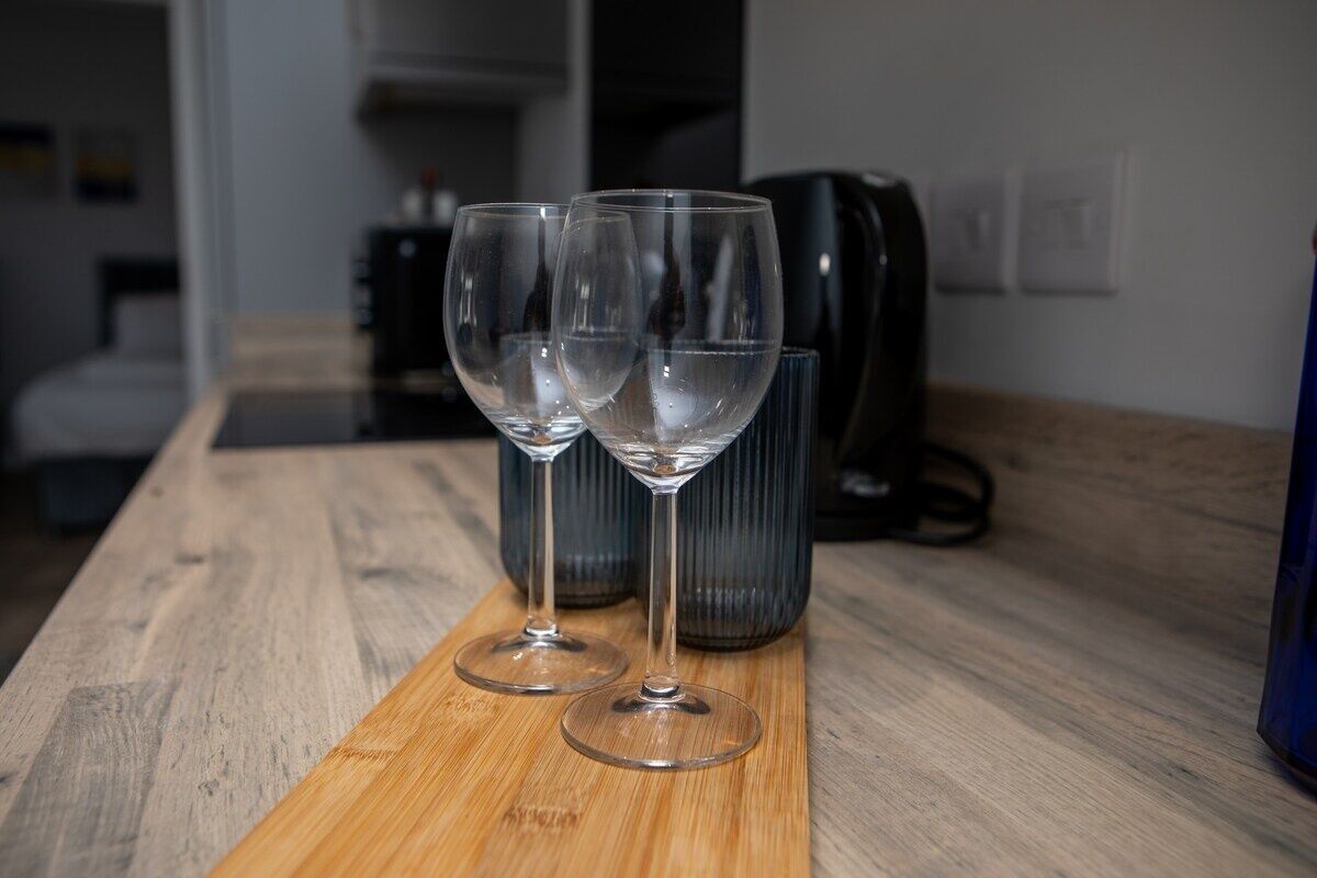 Two empty wine glasses on a wooden table with a coffee maker in the background.