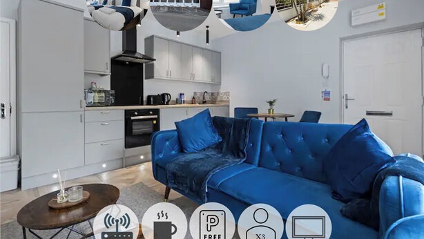 A modern living room with a blue sofa, a coffee table, and a kitchen area with white cabinets and a black stove. - Modern Apartment |King Bed |Free Parking Suite 2 (Nottingham)
