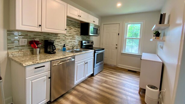 A modern kitchen with white cabinets, stainless steel appliances, and a tiled backsplash. - Charming 2-bedroom Apartment near NoDa, Plaza Midwood, Uptown, and more (Charlotte)