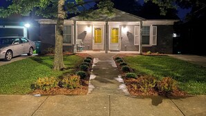 A two-story house with a front porch, a driveway, and a car parked on the left. - Charming 2-bedroom Apartment near NoDa, Plaza Midwood, Uptown, and more (Charlotte)
