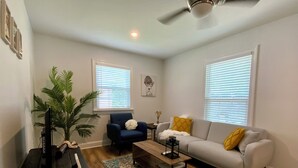 A living room with a sofa, armchair, coffee table, and a TV stand. - Charming 2-bedroom Apartment near NoDa, Plaza Midwood, Uptown, and more (Charlotte)