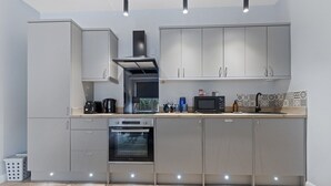 A modern kitchen with grey cabinets, a built-in oven, a microwave, and a coffee maker. - Modern Apartment King Bed| Free Parking| Suite 1 (Nottingham)