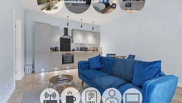 A modern living room with a blue sofa, a coffee table, and a kitchen in the background. - Modern Apartment King Bed| Free Parking| Suite 1 (Nottingham)