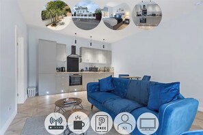 Una sala de estar moderna con un sofá azul, una mesa de centro y una cocina al fondo.