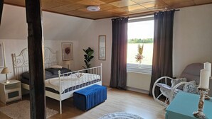Makuuhuoneessa on sänky, yöpöydät, ikkuna verhoineen, patteri ja näkymä vehreään maisemaan.
