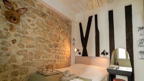 A bedroom with a stone wall, a bed with a green blanket, a teddy bear, and a nightstand with a mirror and lamp. - Cocon Quarters - One Bedroom Villa, Sleeps 2 (Paris)