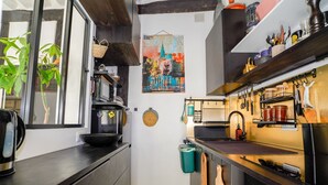 A compact kitchen with a black countertop, a microwave, a kettle, and a stove. There is a hanging basket and a map on the wall. - Cocon Quarters - One Bedroom Villa, Sleeps 2 (Paris)