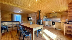 A wooden cabin interior with a dining area, kitchen, and a fireplace. - Datcha at Cap Fréhel (Plévenon)