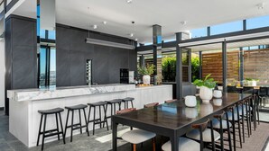 A modern kitchen with a marble countertop, bar stools, and a dining area with a long table and chairs. - Brookstone Penthouse (Cape Town)