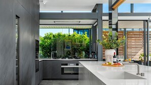 A modern kitchen with a large island, built-in appliances, and a view of greenery through the glass wall. - Brookstone Penthouse (Cape Town)