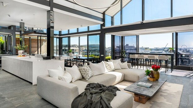 A spacious living area with a large sofa, a coffee table, and a view of the city through large windows. - Brookstone Penthouse (Cape Town)