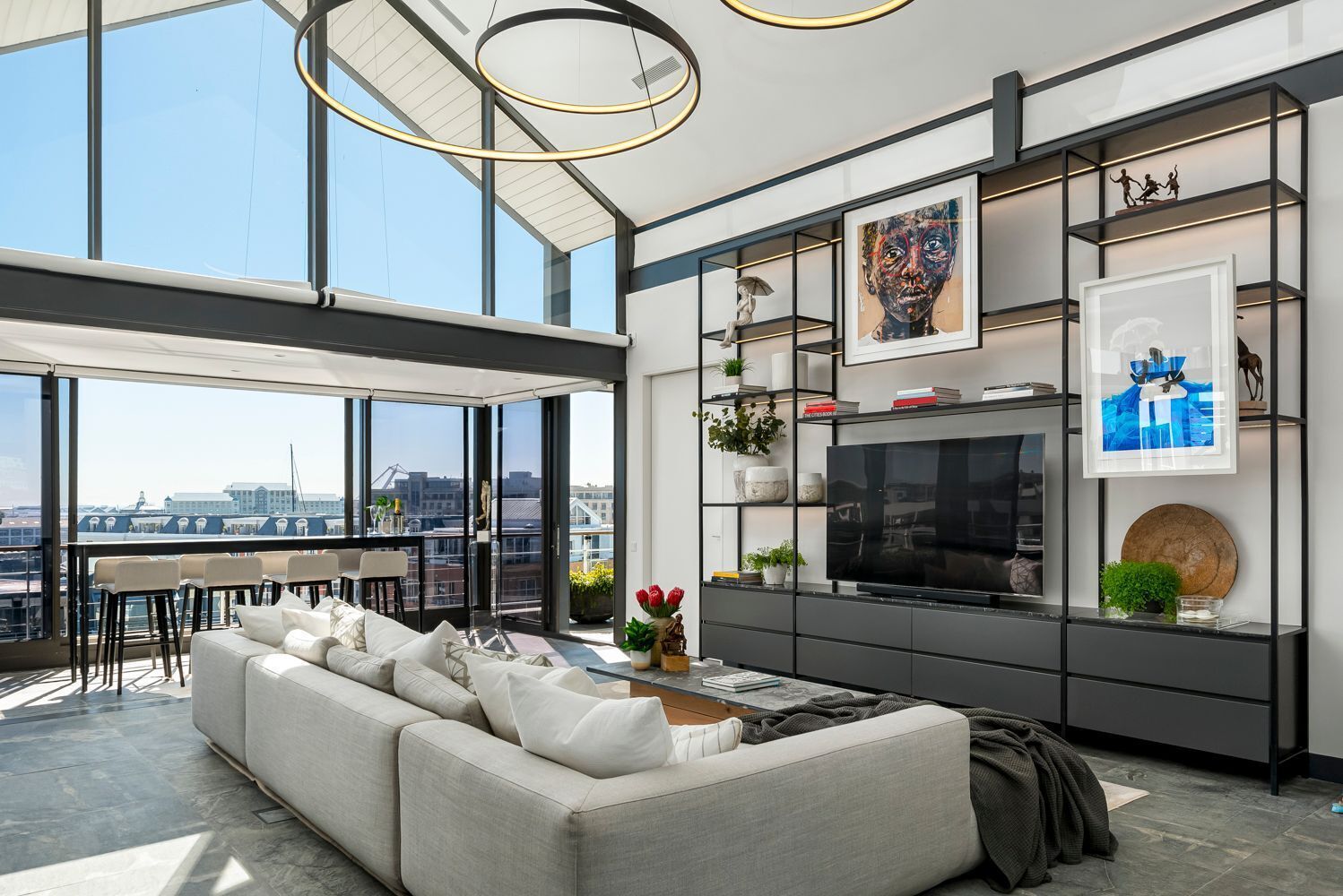 Ein modernes Wohnzimmer mit einer großen Couch, einem Fernseher und Blick auf die Stadt durch große Fenster.