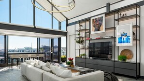 A modern living room with a large sofa, a TV, and a city view through large windows. - Brookstone Penthouse (Cape Town)