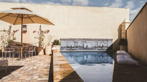 A pool area with a tiled deck, a metal table with chairs, and a large umbrella.