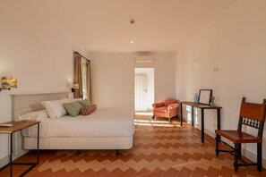 A bedroom with a bed, a nightstand, a chair, a table, and a door leading to another room. - Palacio Catalina - Ten Bedroom Villa, Sleeps 22 (Lora del Río)