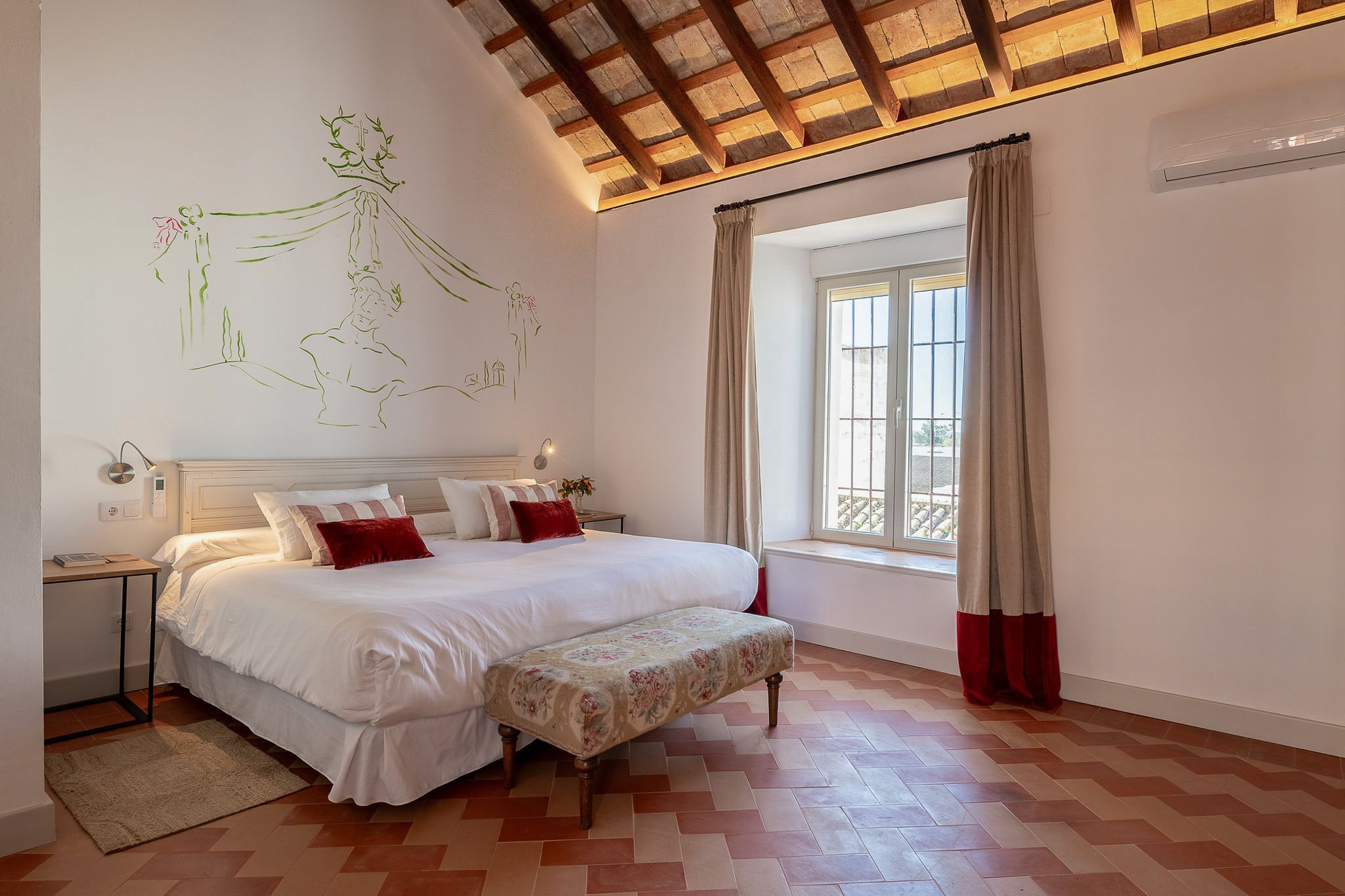 Un dormitorio con cama, mesitas de noche, una ventana con cortinas y una pared con mural.